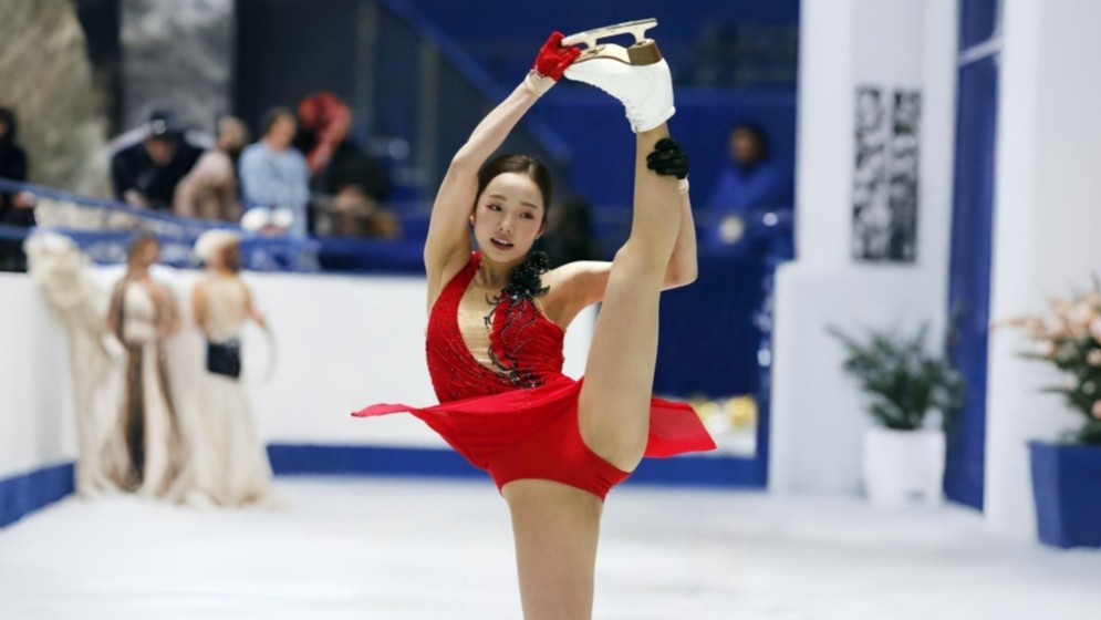 Figure skater with sky-high leg extension in red dress